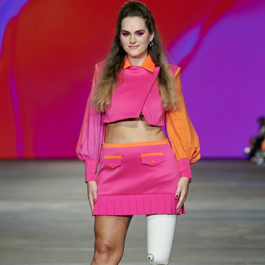 Model with a prosthetic limb wears and hot pink and orange puff sleeve cropped jacket and mini skirt. Christina Stephens Adaptive Clothing Australia. 