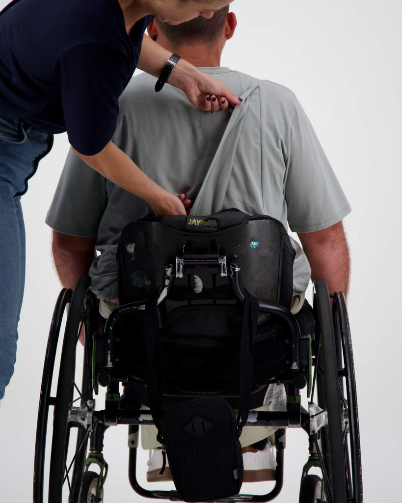 Image of a man sitting in a wheelchair facing backwards. The opening of the back of his prism back t-shirt is being demonstrated. Christina Stephens Adaptive Clothing Australia.