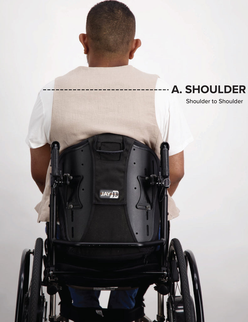 Dark skinned male sits in a wheelchair with a white shirt and a beige vest. Christina Stephens Adaptive Clothing Australia. 
