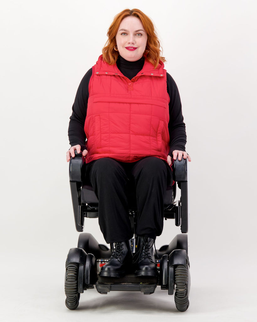 Seated female wearing a red puffer vest over black clothing while seated in a power wheelchair. Christina Stephens Adaptive Clothing Australia. 