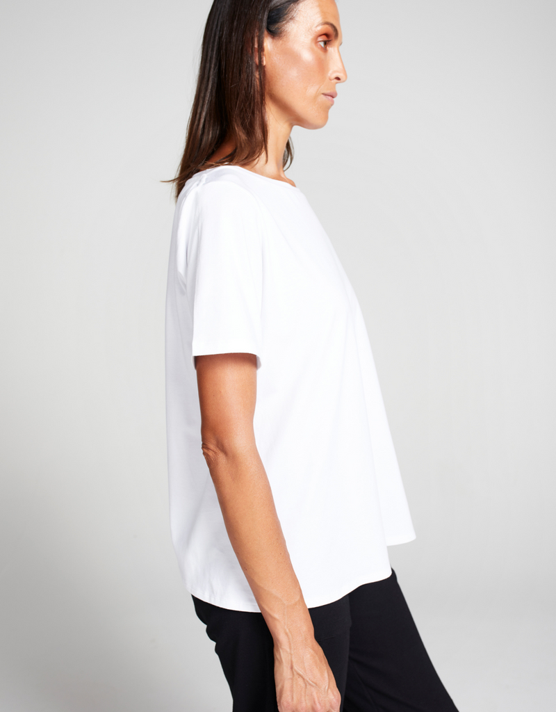 Woman with dark hair wearing a white short sleeve t-shirt. Standing. Side facing.