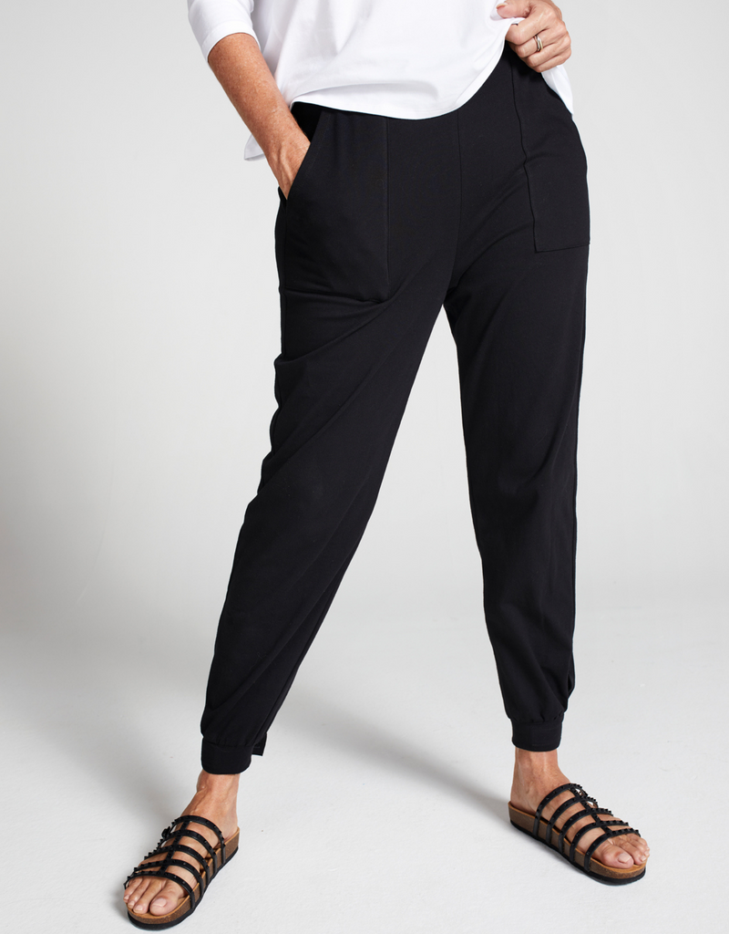 Woman wearing black tapered leg pants with square pocket detail, cuff at leg opening and black sandals. 
