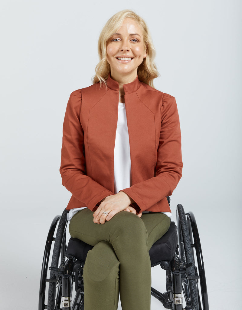 Image of a blonde female in a wheelchair wearing a brick red jacket, white t-shirt and khaki leggings. Christina Stephens Adaptive Clothing Australia. 
