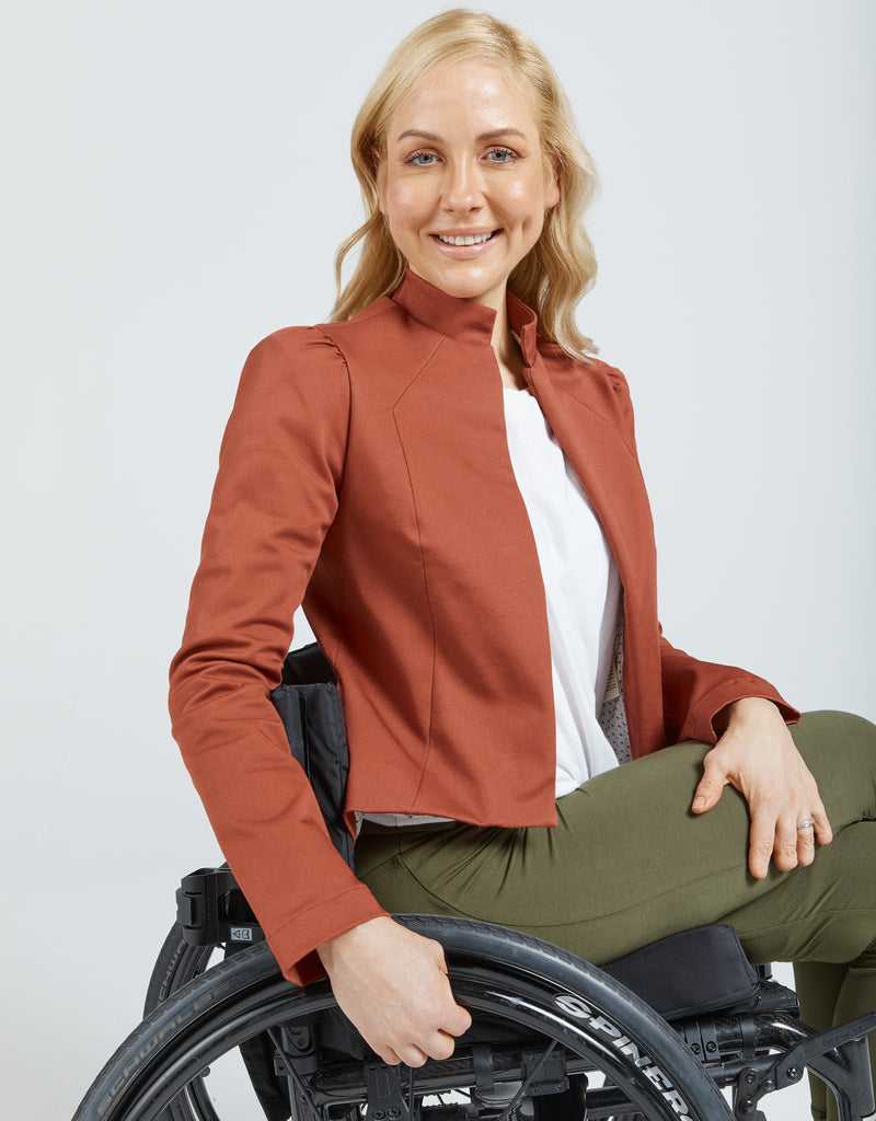 Image of a blonde female in a wheelchair wearing a brick red jacket, white t-shirt and khaki leggings. Christina Stephens Adaptive Clothing Australia. 
