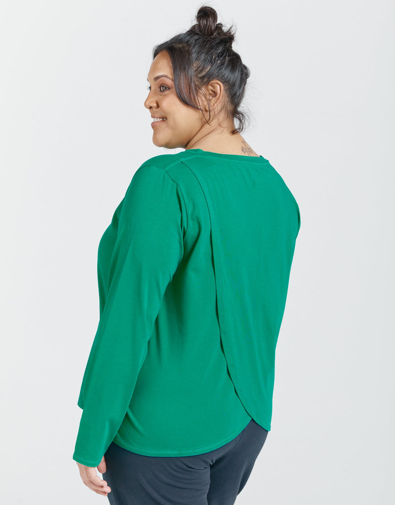 Image of a standing female wearing a long sleeve, pea green t-shirt. Christina Stephens Adaptive Clothing Australia.