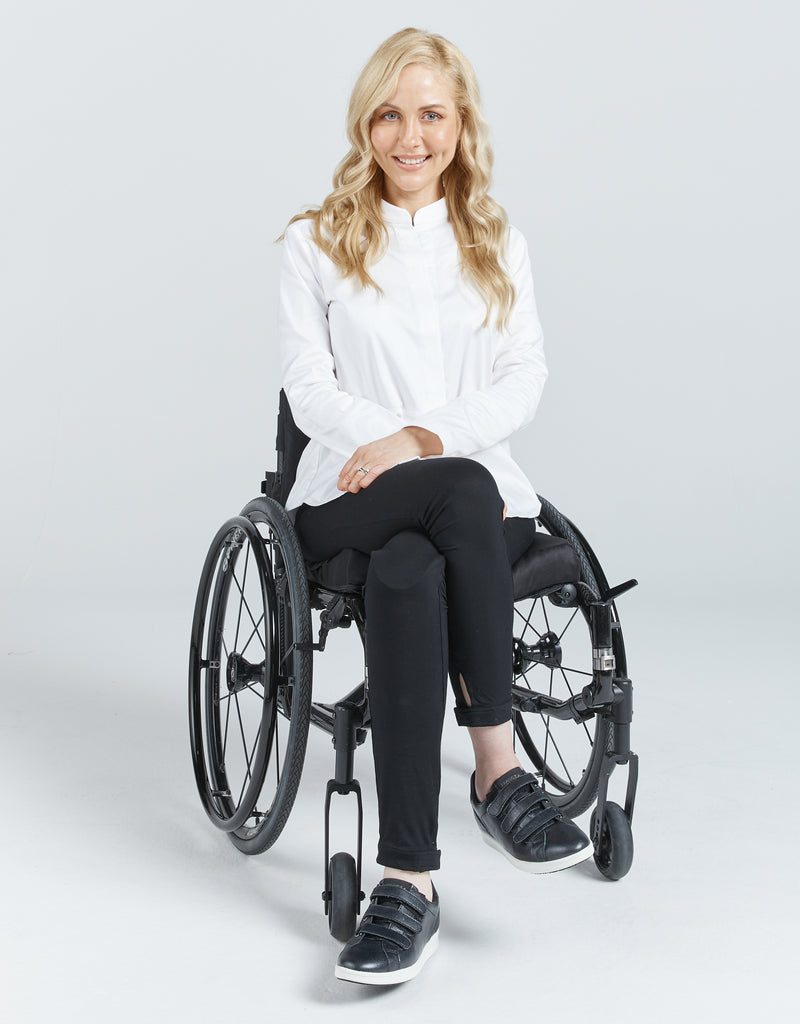 Blonde female in a wheelchair wearing a white shirt with a Chinese collar, black leggings and black sneakers. She is smiling. Christina Stephens Adaptive Clothing Australia. 