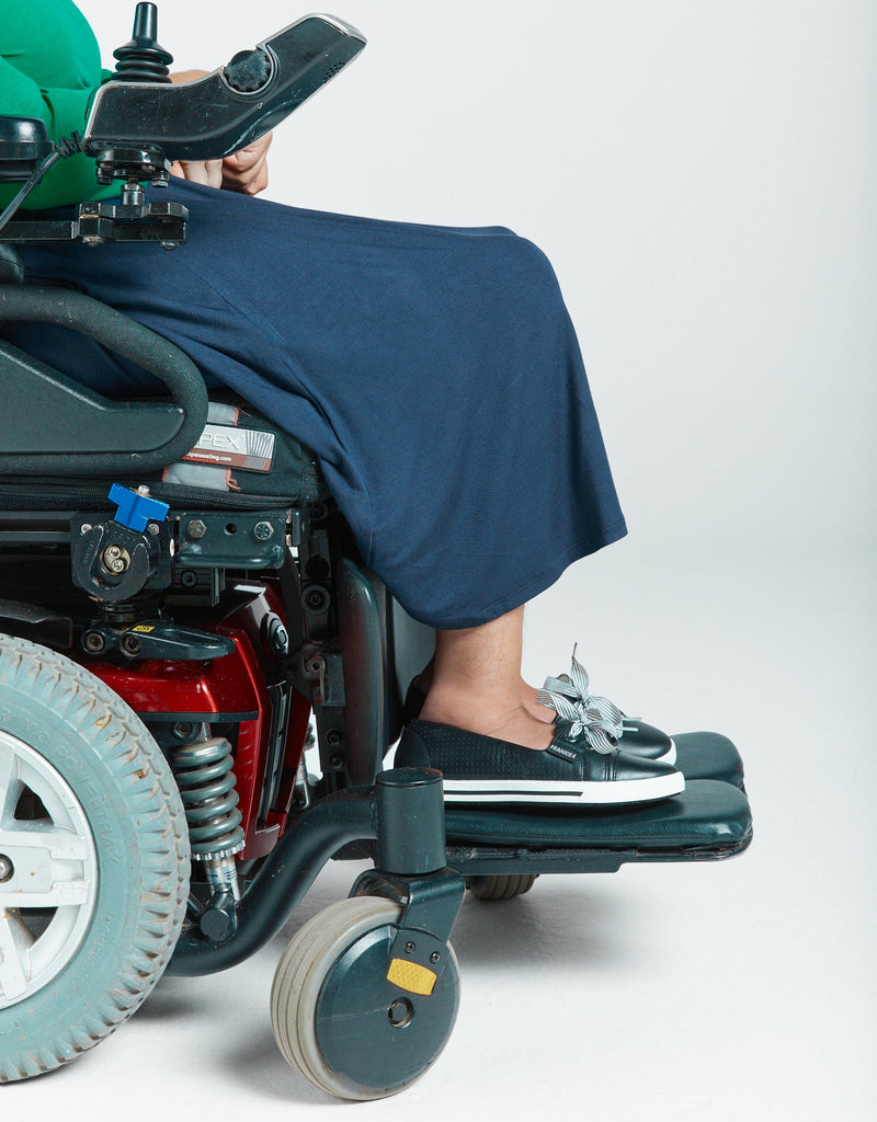 A lady in a power wheelchair is wearing a navy bamboo skirt that reaches to just above her ankles (as she is seated). She is wearing a green top and black shoes. Christina Stephens Adaptive Clothing Australia. 