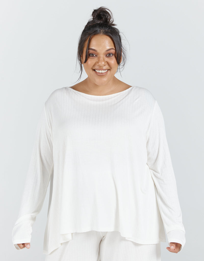 Image of a dark haired, dark skinned standing female, wearing a cream long sleeve top and cream cropped wide leg pants.Christina Stephens Adaptive Clothing Australia.