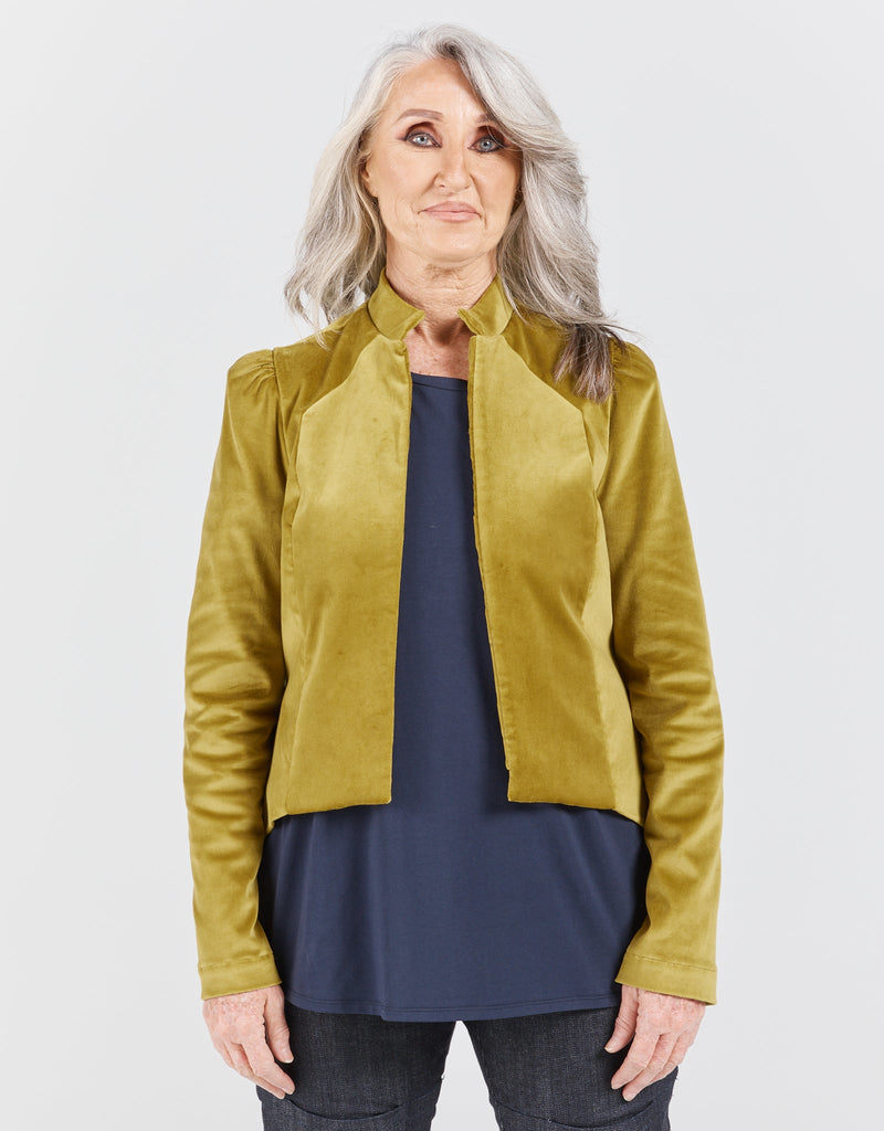 Image of a standing female with grey hair, wearing a citrus green velvet jacketing, a navy top and blue denim jeans. Christina Stephens Adaptive Clothing Australia. 