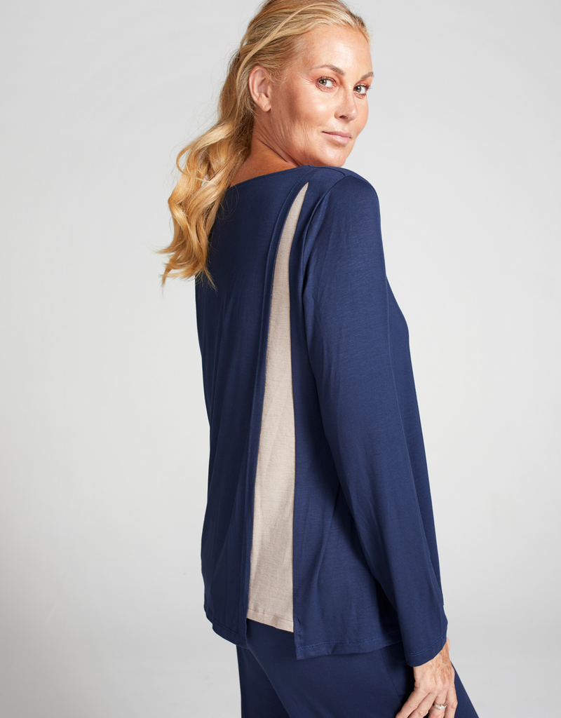 Blonde woman wearing a blue loose fitting, long sleeve top with rounded neckline.  Standing. Side facing. 