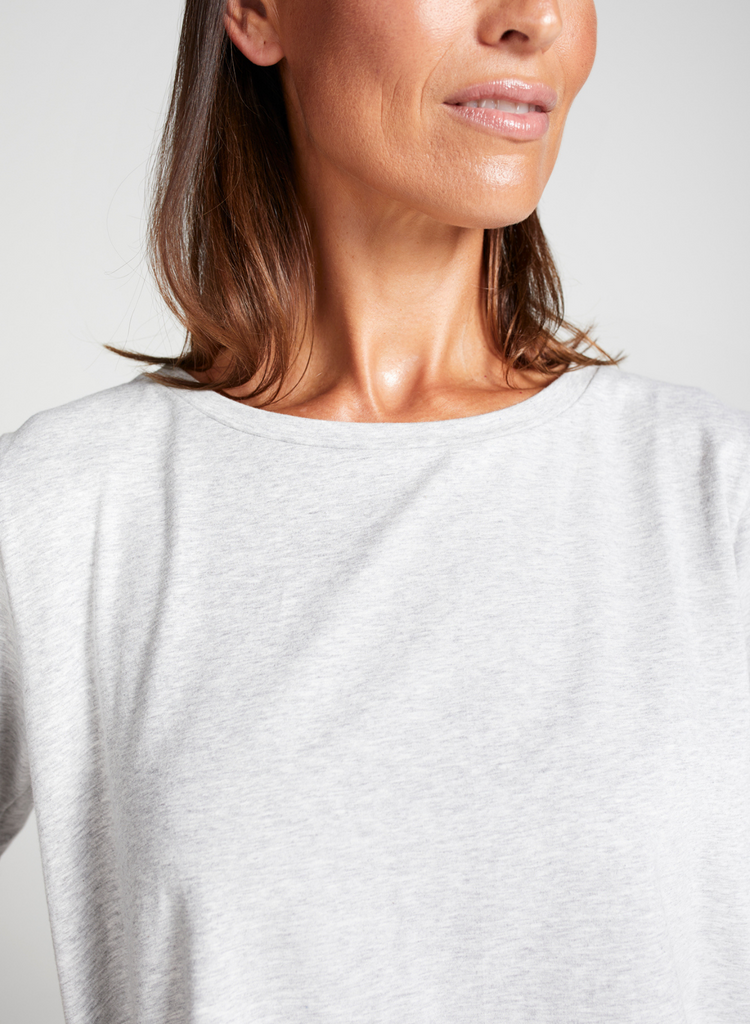 Brunette woman wearing a short sleeve grey marle t-shirt. Standing. Forward facing. Top of garment and face in focus.