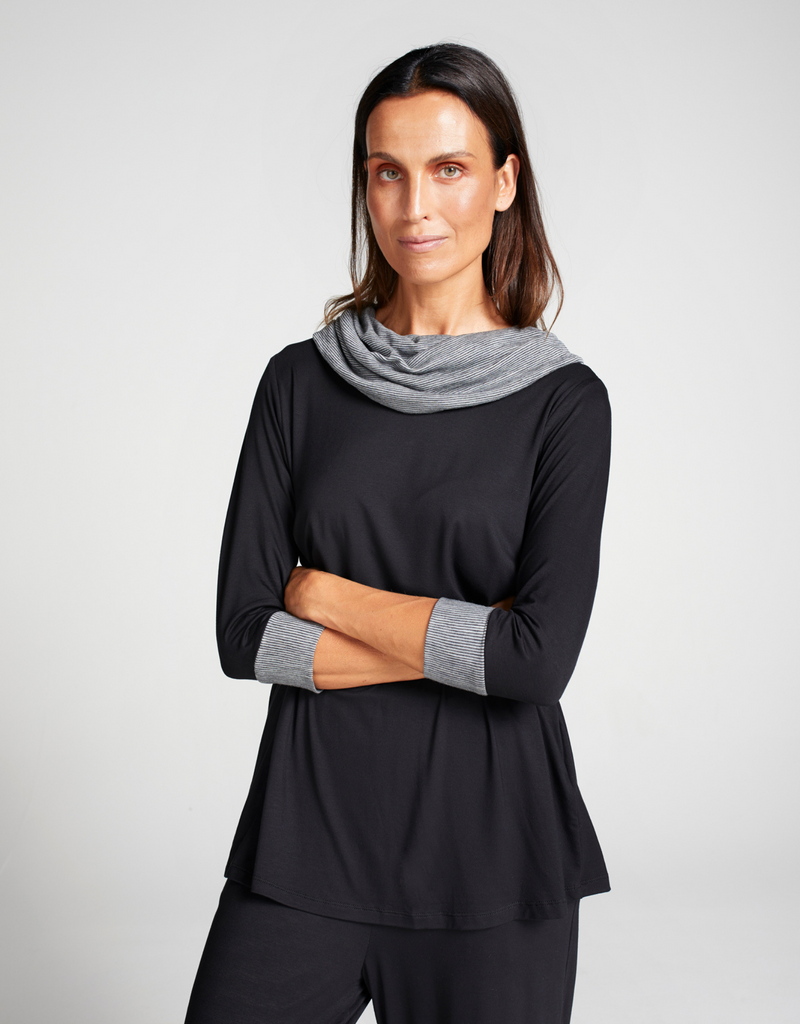Woman wearing black, bamboo leaf back top with grey stripe cowl neck and sleeve cuffs. Standing. Forward facing. 