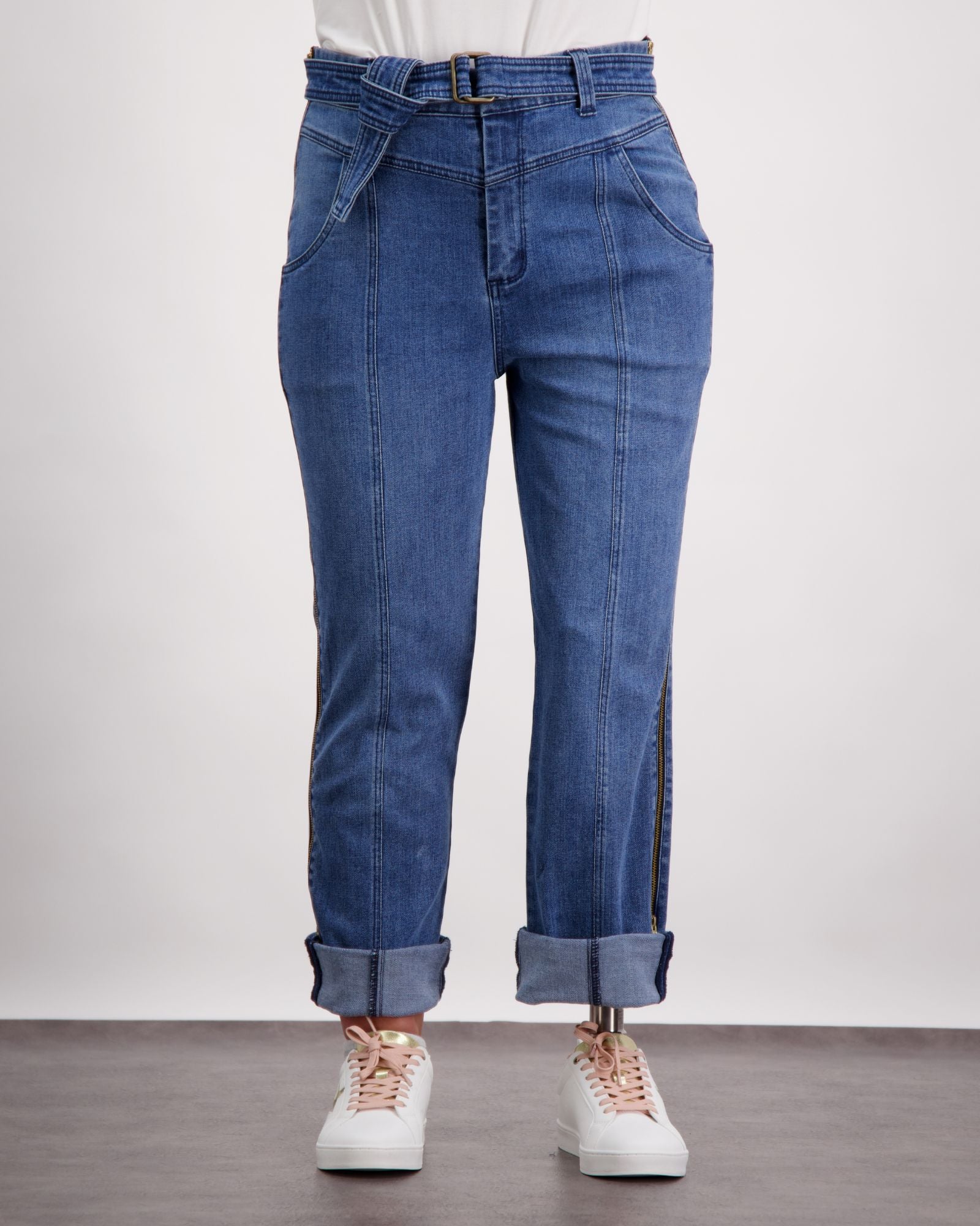Christina Prosthetic Jeans featured in medium-wash denim with side zippers, rolled cuffs, and innovative tear-resistant fabric. Displayed with white sneakers against a light background, showcasing adaptive design elements and comfortable fit.