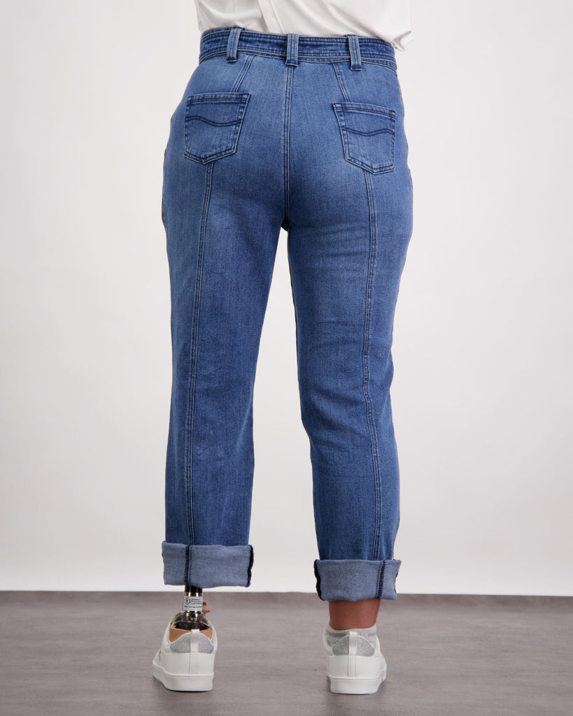 Female wearing a blue and white t-shirt and blue jeans is standing with white sneakers on her prosthetic foot. She is facing to the back. Christina Stephens Adaptive Clothing Australia. 