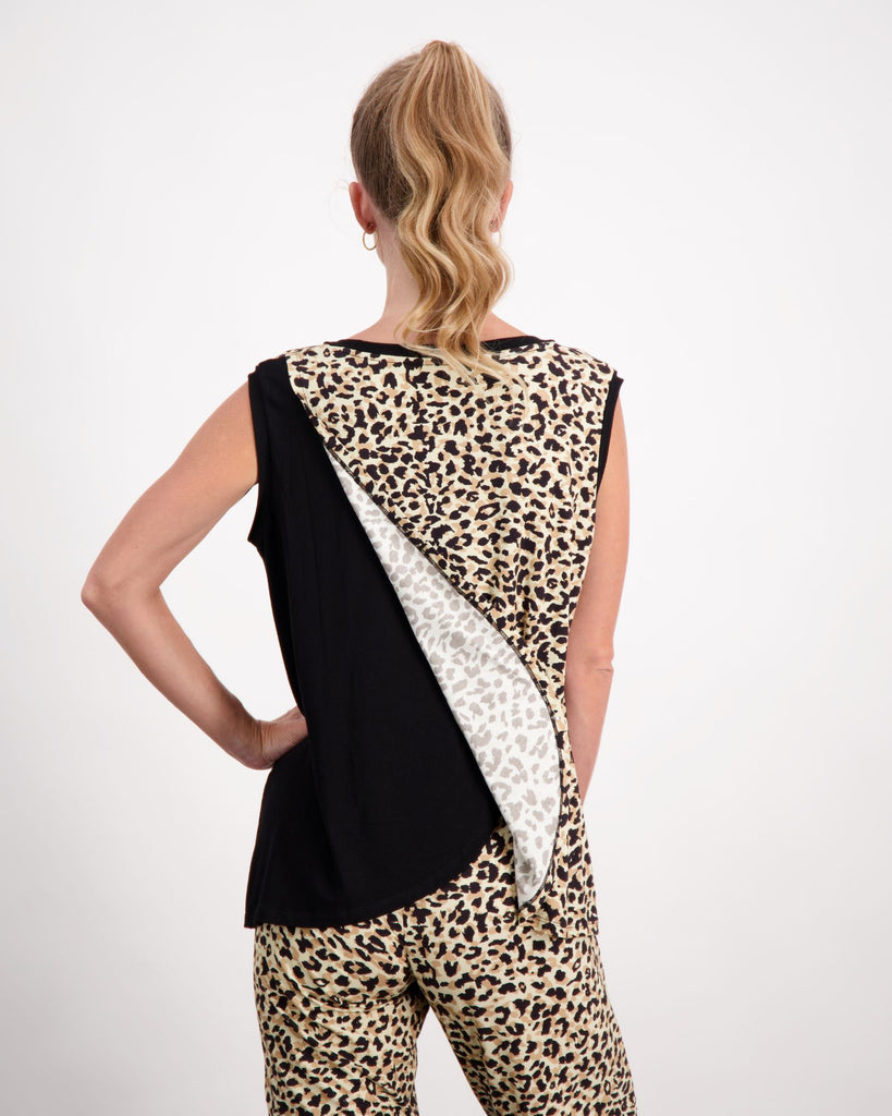 A standing blonde female wearing a pony-tail is wearing a black and leopard print bamboo sleeveless physio top.  She is facing towards the back of the room to highlight the leaf back design of the top. The back of the top has an upper leaf that is leopard print and the bottom leaf is black fabric. The back leaf is slightly opened to demonstrate the opening functionality of the back of the top. She has paired the top with matching leopard print bamboo pants. Christina Stephens Australian Adaptive Clothing. 