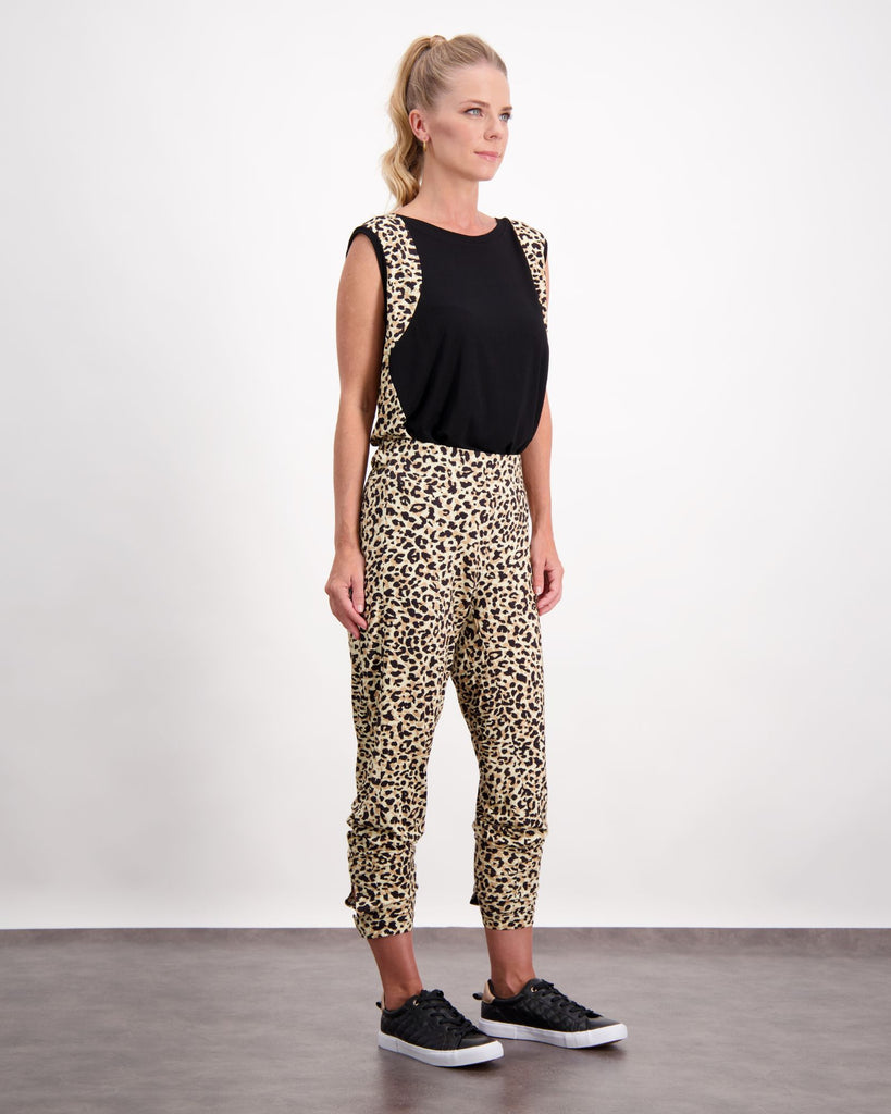 A standing blonde female with blue eyes wearing a pony-tail is wearing a black and leopard print bamboo sleeveless physio top. The leopard print highlights the black front of the top. She has paired the top with matching leopard print bamboo pants and is wearing black leather running shoes. Christina Stephens Australian Adaptive Clothing. 