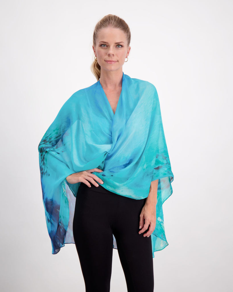 Blonde standing female is wearing a silk, aqua blue print kaftan with small pearl buttons, black leggings and black boots. Christina Stephens Adaptive Clothing Australia. 