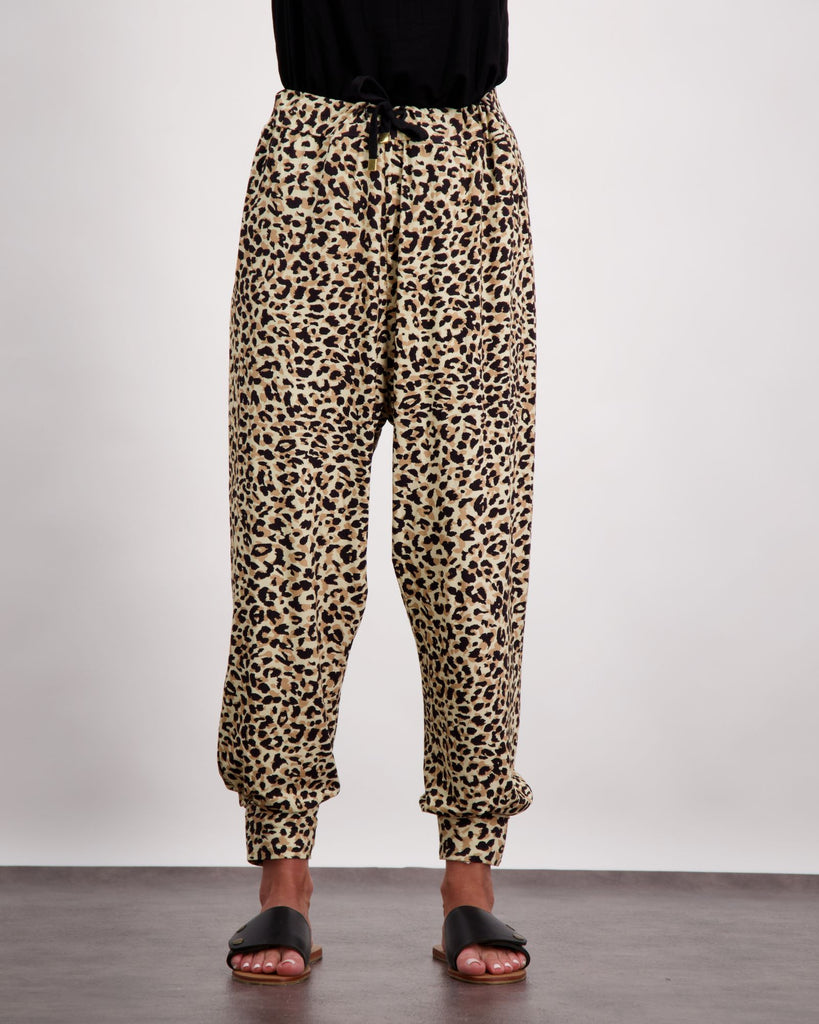 An image of a standing female wearing leopard print slouch pants with a black draw string and black leather slippers. The bottom of her black top is visible. Chistina Stephens Adaptive Clothing Australia. ﻿