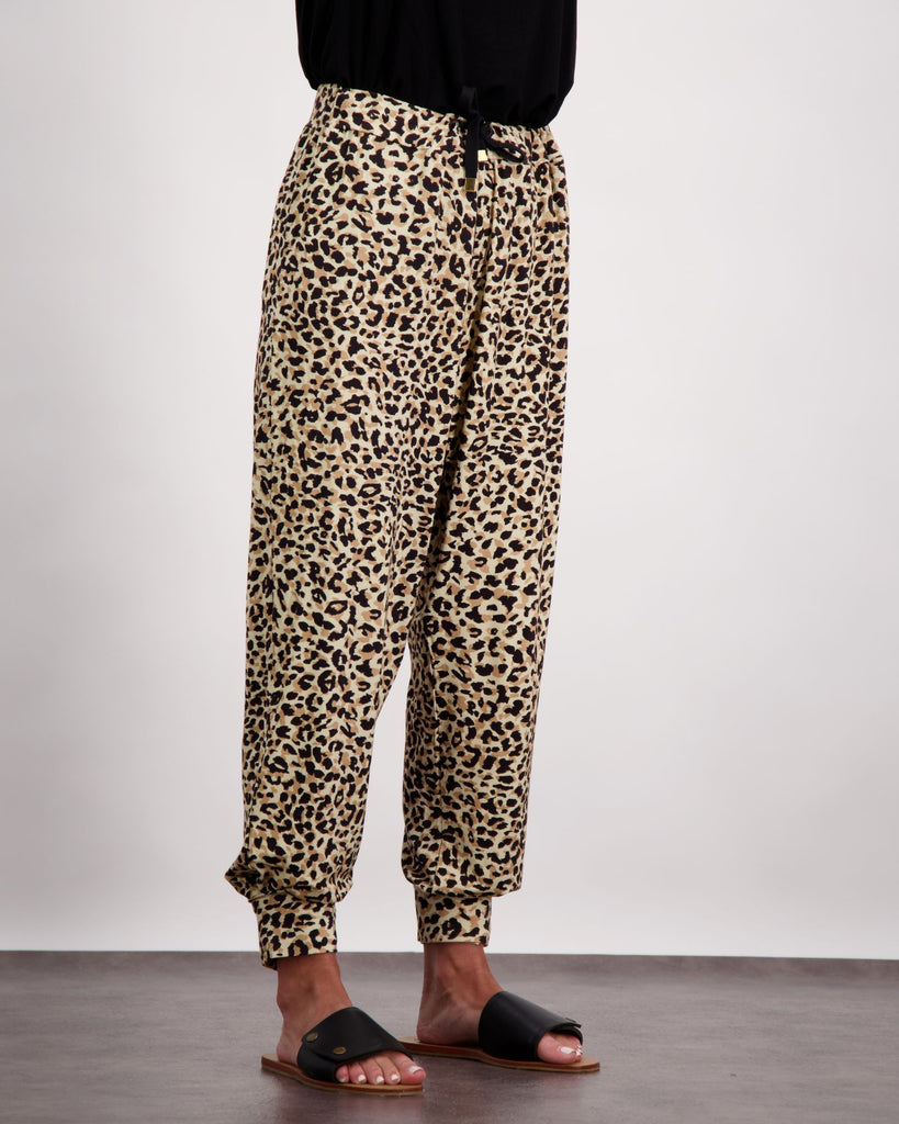 An image of a standing female wearing leopard print slouch pants with a black draw string and black leather slippers. The bottom of her black top is visible. Chistina Stephens Adaptive Clothing Australia. 