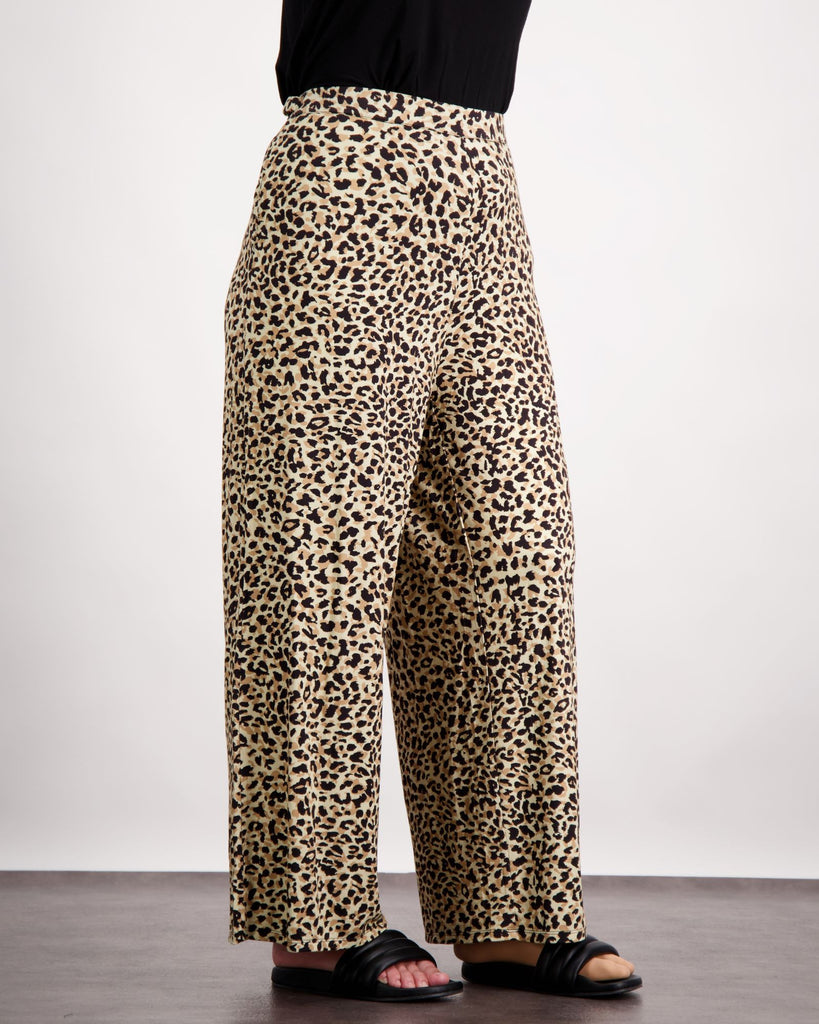 Image is of a female wearing a pair of leopard print bamboo wide leg pants and black leather slippers. She is facing side-on. The bottom of her black top is visible. Christina Stephens Australian Adaptive Clothing.