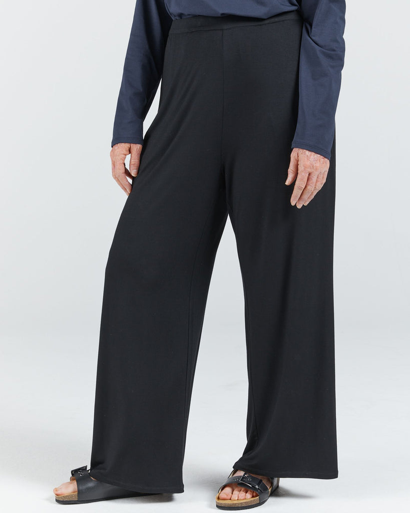 Image is of a female wearing a pair of black bamboo wide leg pants, a navy long sleep leaf-back t-shirt and black leather slippers. Christina Stephens Australian Adaptive Clothing.