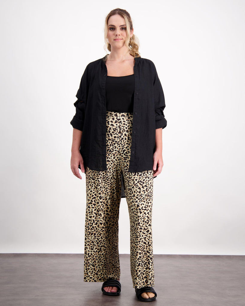 A standing female with caucasian skin and sandly coloured curly hair is wearing a black camisole under a black open linen shirt. She is wearing leopard print wide leg pants and black leather slippers. Christina Stephens Australian Adaptive Clothing. ﻿