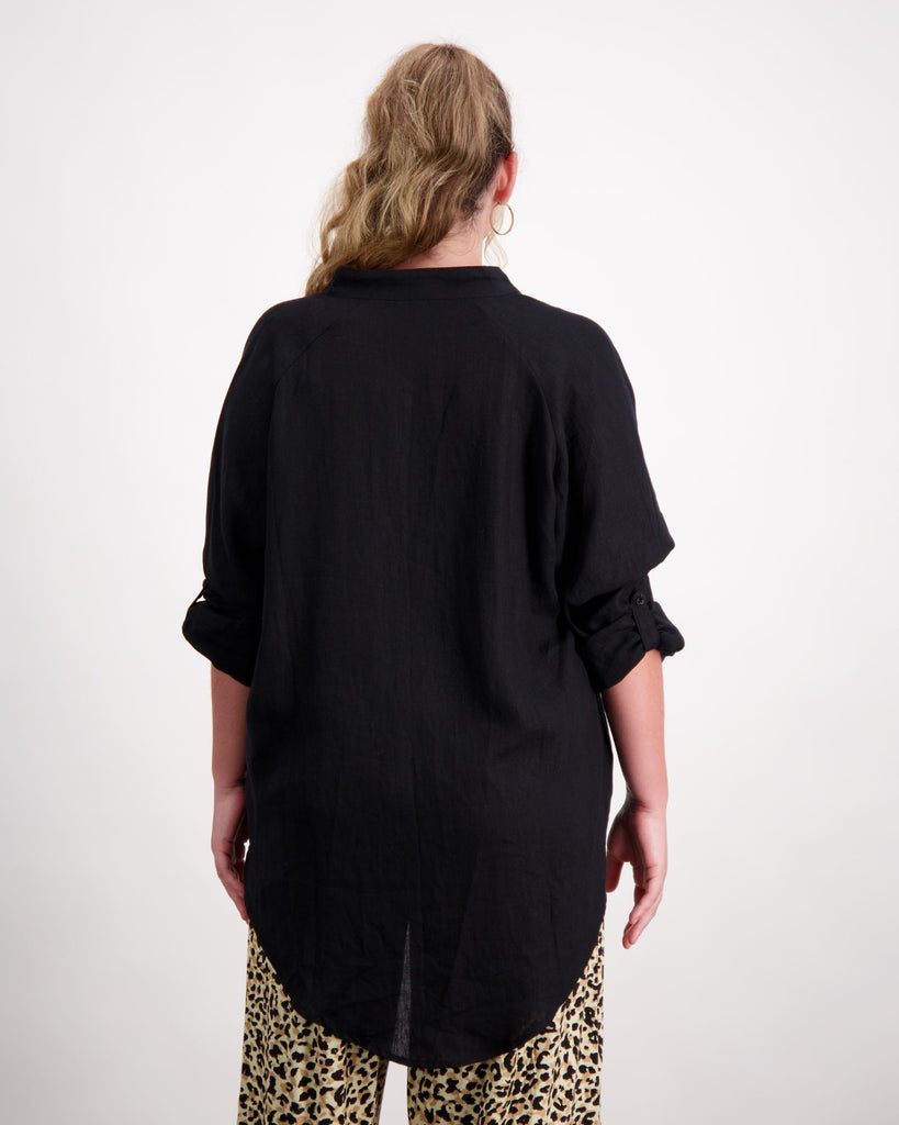 A standing female with caucasian skin and blonde curly hair is wearing a black linen shirt with leopard print wide leg pants. She is facing with her back to the camera. Christina Stephens Australian Adaptive Clothing. 