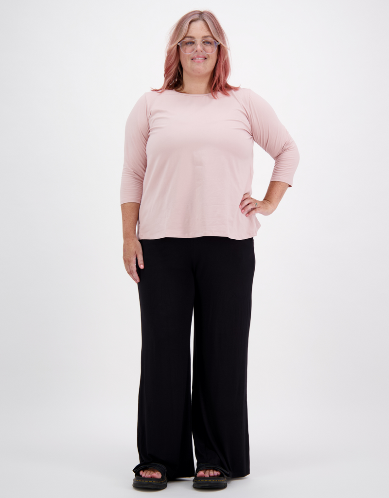 Woman with pink hair and glasses is wearing a light pink 3/4 sleeve leaf back t-shirt, black trousers and black platform sandals. She is facing the front. Christina Stephens Adaptive Clothing Australia. 