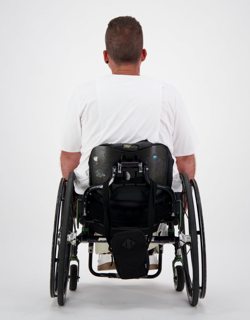Man with light brown, short hair, is in a wheelchair wearing a white t-shirt and and facing to the back to display the prism back on the t-shirt. Christina Stephens Australian Adaptive Clothing. 