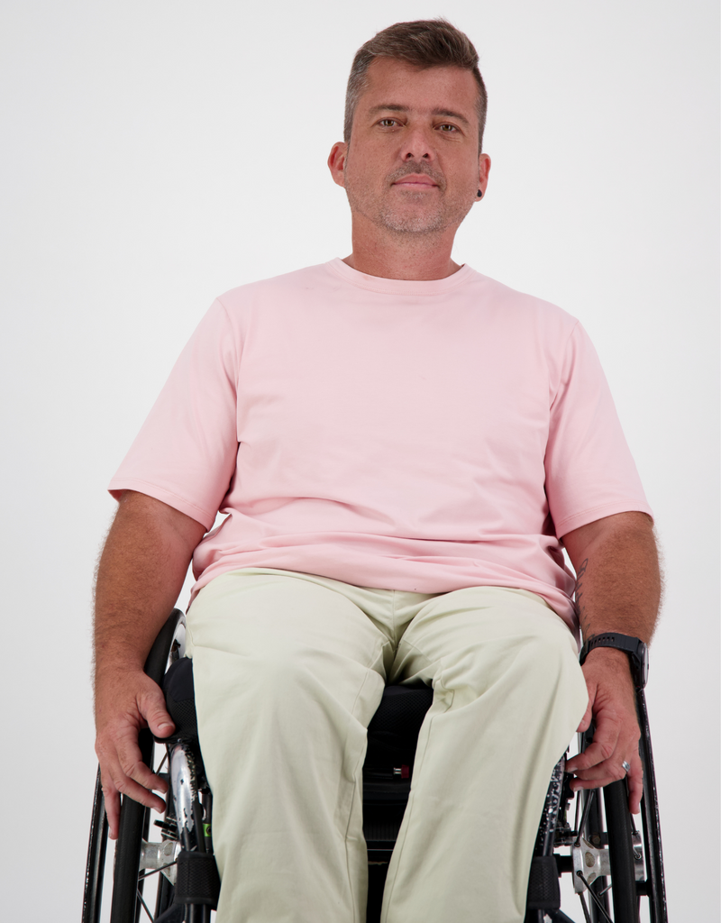 Man with light brown, short hair, is in a wheelchair wearing a pink t-shirt and cream cargo pants. Christina Stephens Australian Adaptive Clothing. 