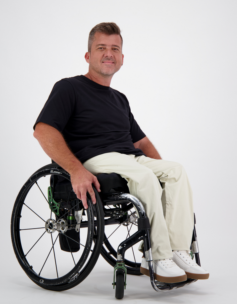 Man with light brown, short hair, is in a black t-shirt and cream cargo pants. Christina Stephens Australian Adaptive Clothing. 