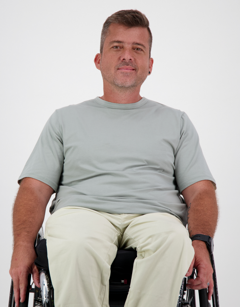 Man with light brown, short hair, is in a khaki t-shirt and cream cargo pants. Christina Stephens Australian Adaptive Clothing. 