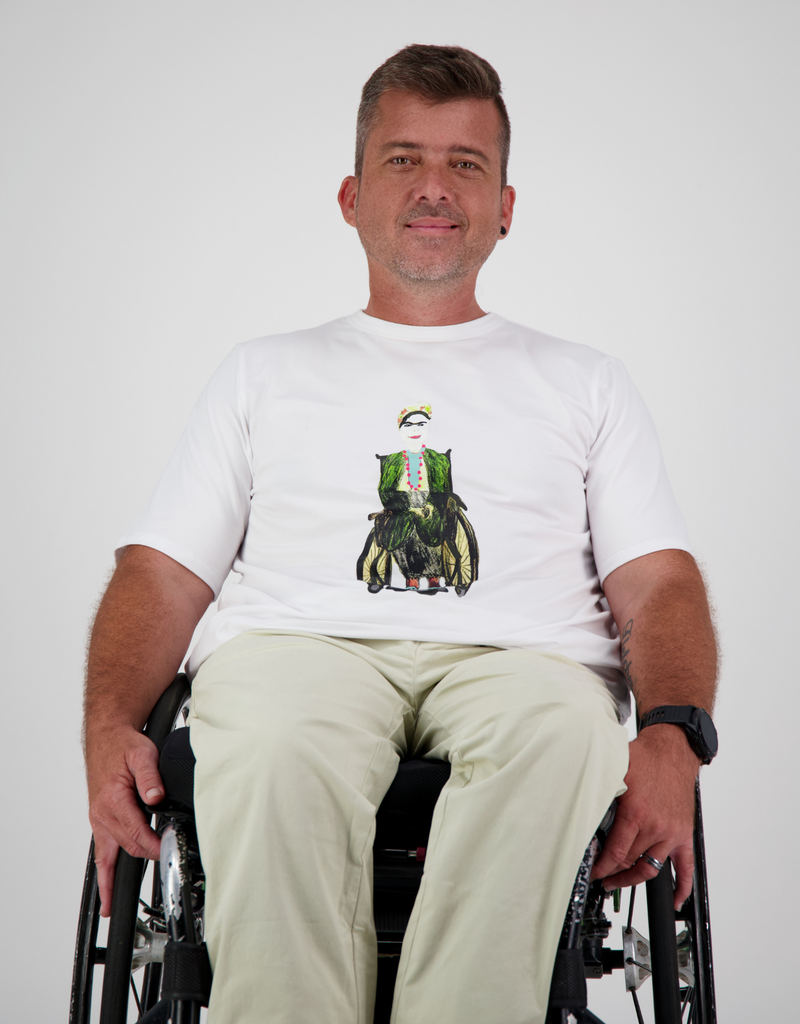 Man with light brown, short hair, is in a white prism back t-shirt with bespoke art work of FRIDA and cream cargo pants. Christina Stephens Australian Adaptive Clothing. 